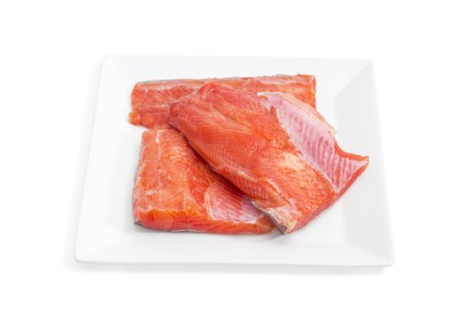 Several pieces of fresh uncooked fillet of rainbow trout on a square dish on a light background closeup