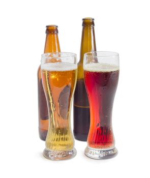 Two beer glasses with lager beer and dark beer against of beer bottles on a light background
