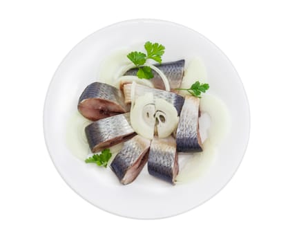 Sliced pickled atlantic herring, chopped onions and parsley leaves on a white dish on a light background
