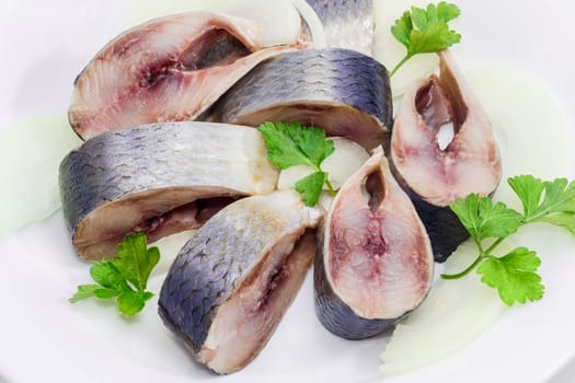 Sliced pickled atlantic herring, chopped onions and parsley leaves on a white dish closeup
