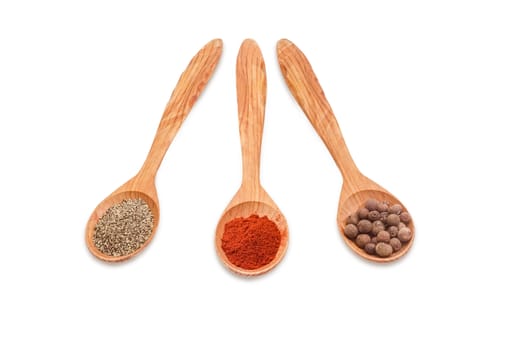 Three wooden spoons of various kinds of pepper - ground black pepper, chili powder and allspice on a light background 
