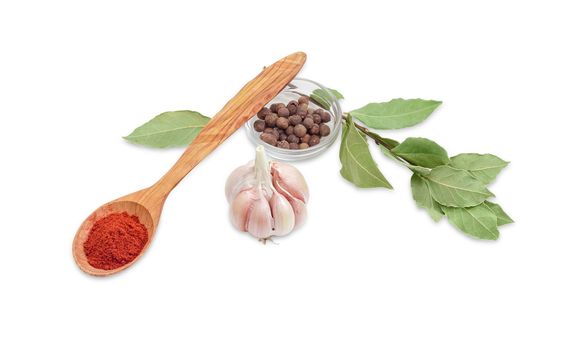 Wooden spoon with chili powder, small glass container of allspice, bulb of a garlic and branch with a dried bay leaves on a light background 
