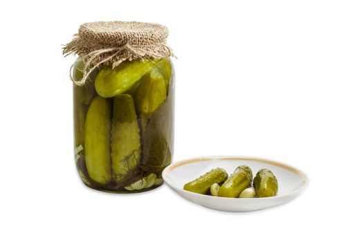 Homemade pickled cucumbers in glass jar and several pickled cucumbers with garlic on a saucer on a light background
