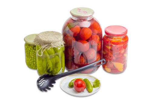 Two pickled cucumbers and one pickled tomato on a saucer, pickled cucumbers, tomatoes, bell pepper and green peas in glass jars and black plastic slotted spoon on a light background
