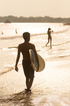 Silhouette of male surfer on the beach with the surfboard in sunset.