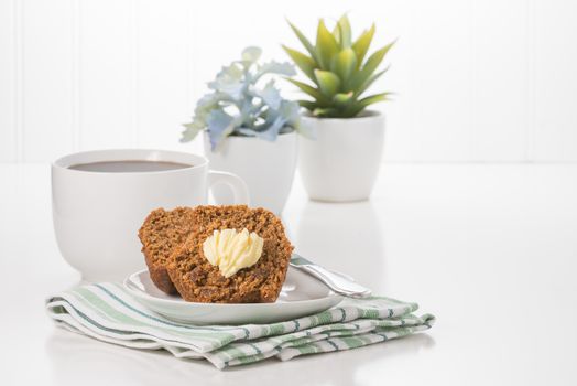 Fresh bran muffin with butter served with coffee.