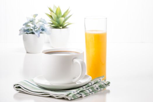 Cup of hot coffee and glass of orange juice with potted plants in background.