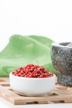 Bowl of pink whole peppercorns with a small part of a mortar and pestle in the background.