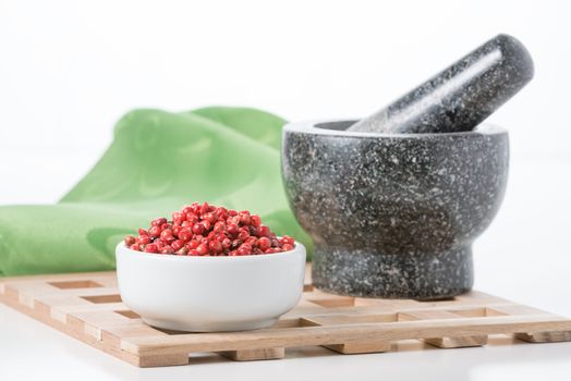 Bowl of whole pink peppercorns with a mortar and pestle in the background.