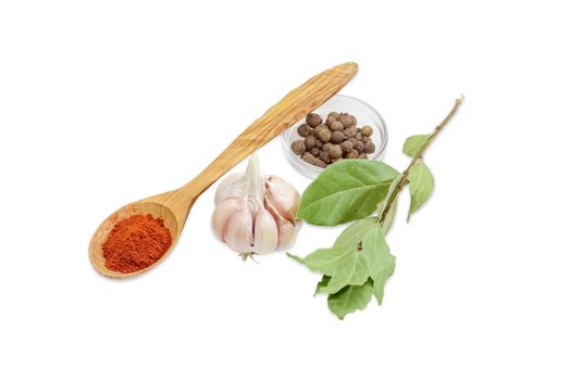 Wooden spoon with chili powder, small glass container of allspice, bulb of a garlic and branch with a dried bay leaves on a light background 
