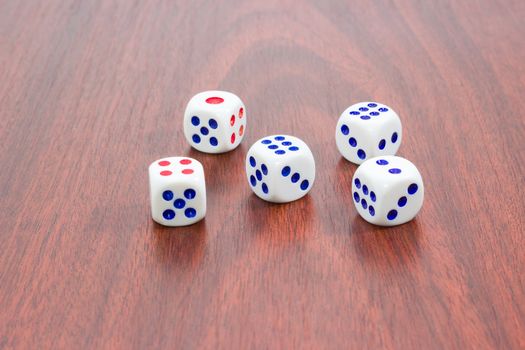 Five traditional plastic white six-sided dice with red and blue dots and rounded corners on wooden surface
