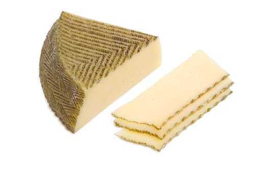 Piece and several slices of semi-hard Spanish cheese with dark coating manufactured from mixtures of cow and sheep milk on a light background
