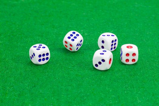 Traditional plastic white six-sided dice with red and blue dots and rounded corners on a table covered with green cloth closeup
