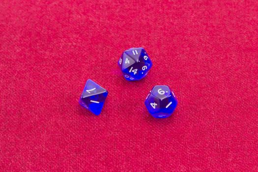 Three blue specialized polyhedral dice with numbers used in role-playing games on table with red cloth
