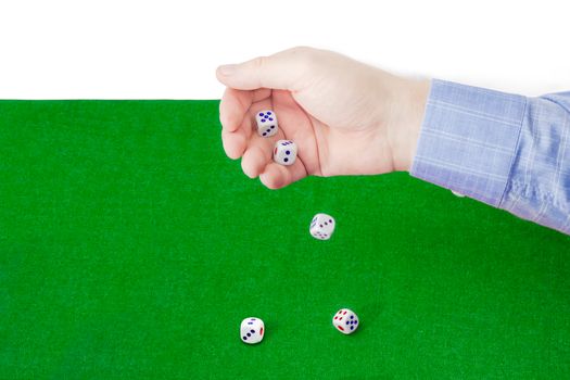 Traditional plastic white six-sided dice with red and blue dots thrown from a male hand on the table with green cloth on a light background. 
