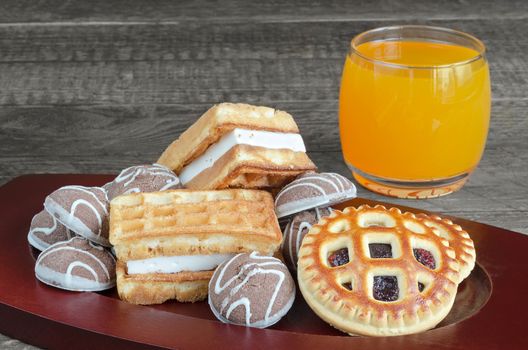 Different cookies and orange juice in a glass on wooden background. Selective focus.