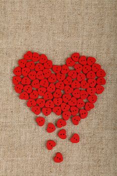 Red heart shaped handmade wooden sewing buttons form broken heart on linen canvas with copy space left, elevated top view