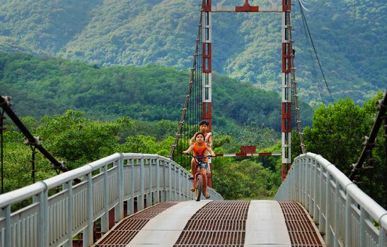 LAM DONG, VIET NAM- JAN 1, 2017: Group of unidentified Vietnamese children ride bicycle cross suspension bridge at countryside, beautiful scene with green forest at Lamdong, Vietnam