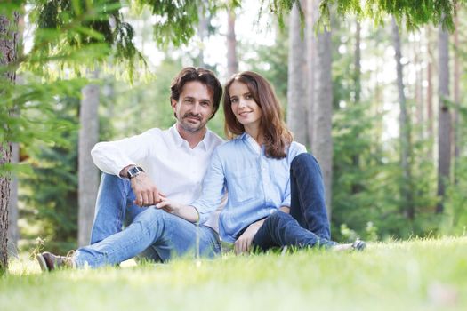 Happy couple sitting on grass in summer park