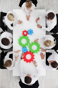 Business team sitting around the table with cogs, teamwork concept