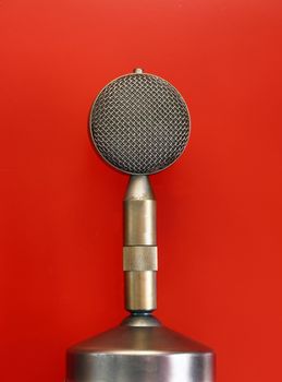 Vintage old retro round vocal metal microphone side view close up over red background