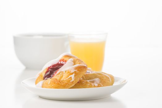 Fresh raspberry danish served with coffee and orange juice against a white background.