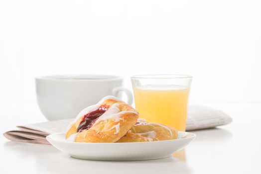 Fresh raspberry danish with coffee and a newspaper in the background.