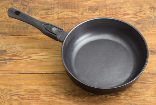 Modern cast frying pan, made of aluminum alloy with ceramic non-stick coating and removable handle on an old wooden surface
