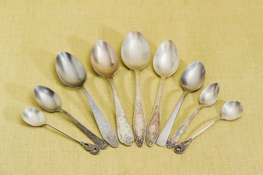 Several old spoons different sizes, made from stainless steel and nickel silver on cloth surface
