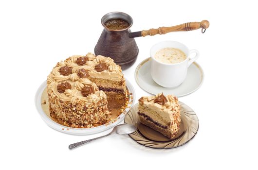 Partly sliced layered sponge cake, decorated with butter cream, caramelized condensed milk and nuts, white cup of a coffee with cream, freshly brewed coffee in old coffee pot on a light background
