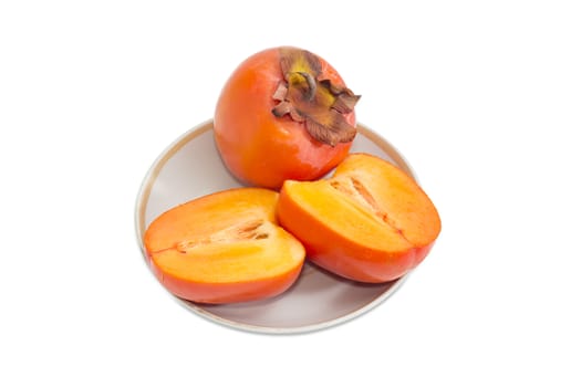 One whole ripe fresh persimmons and one cut in half of a persimmon on saucer on a light background
