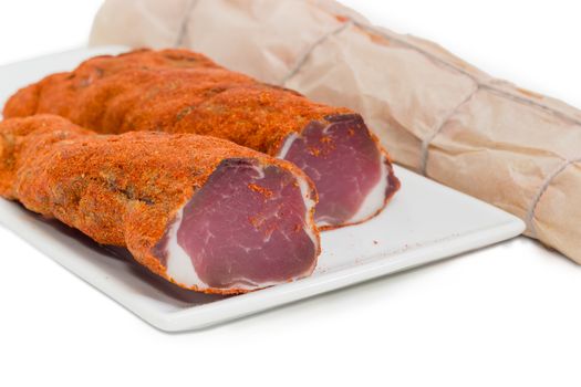 Two pieces of dried pork tenderloin on a white dish closeup and beside it dried pork tenderloin wrapped in parchment paper on a light background 
