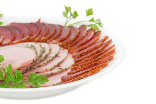 Fragment of white dish with sliced dried pork tenderloin, ham and twigs of parsley closeup on a light background 
