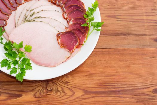 Fragment of white dish with sliced dried pork tenderloin, ham and twigs of parsley closeup on a light background 
