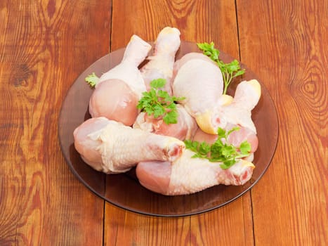 Uncooked chicken legs and twigs of parsley on a glass dish on an old wooden surface
