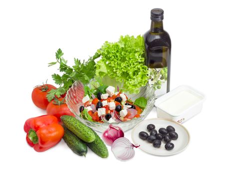 Greek salad in a glass salad bowl among ingredients for its cooking on a white background. 
