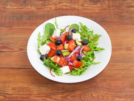 Greek salad in a white dish on an old wooden surface
