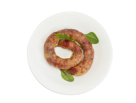 Top view of freshly roasted pork sausage in natural casing with few leaves of different leafy greens on a white dish on a light background
