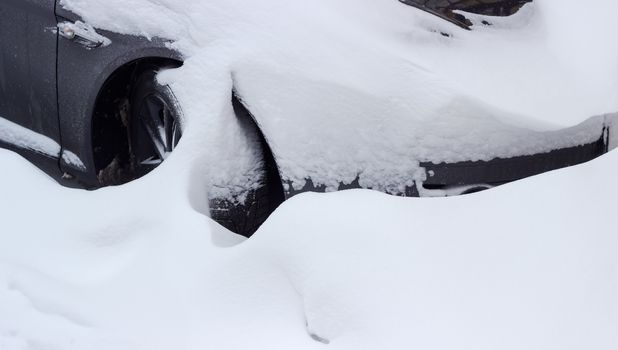 Fragment of the black car with a front wheel, heavily covered with snow during snowfall
