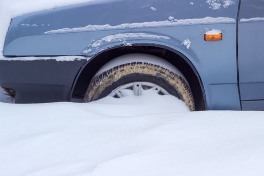 Fragment of the snow covered blue car with a front wheel tire covered with mud
