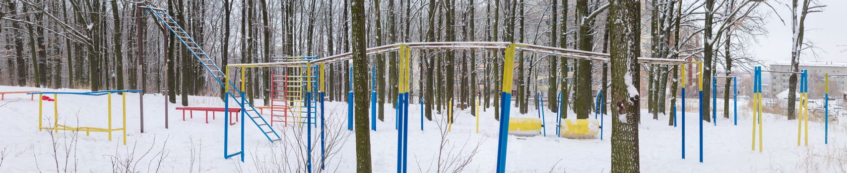 Panorama of outdoor gym in winter public park near the residential area
