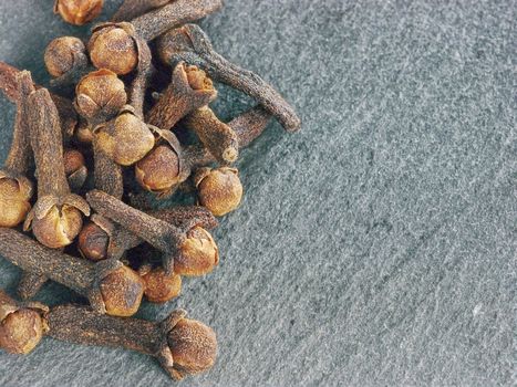 Cloves spice on gray slate background with copy space. Isolated one edge. Top view or flat lay.