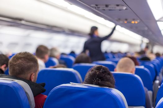 Interior of airplane with passengers on seats and stewardess walking the aisle.