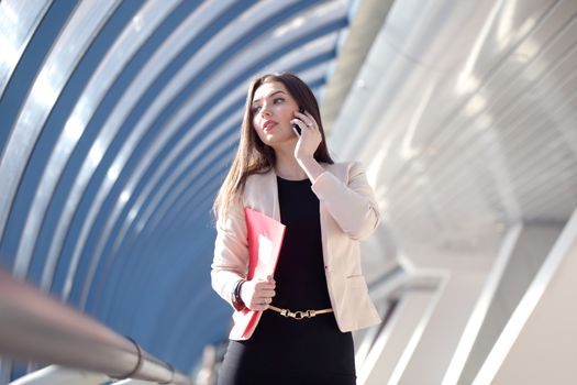 Young Businesswoman with folder talking on the phone in modern building