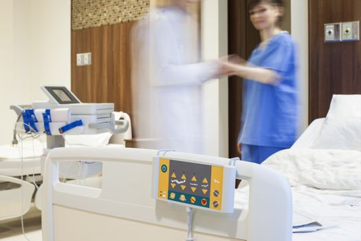 Blurred figures of doctor measuring the pulse of a patient in modern hospital room.