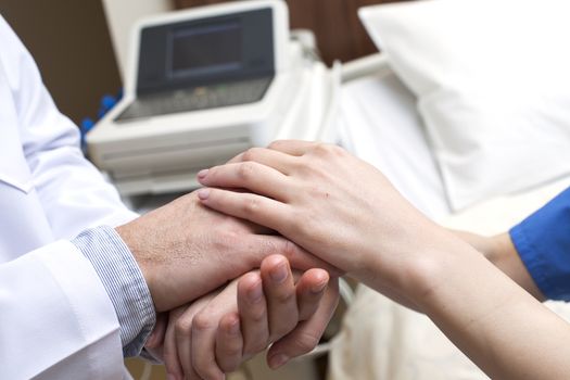 Close-up of doctor holding patient's hands in hospital.