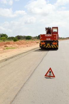 Portable danger road sign on track with transport of construction machinery