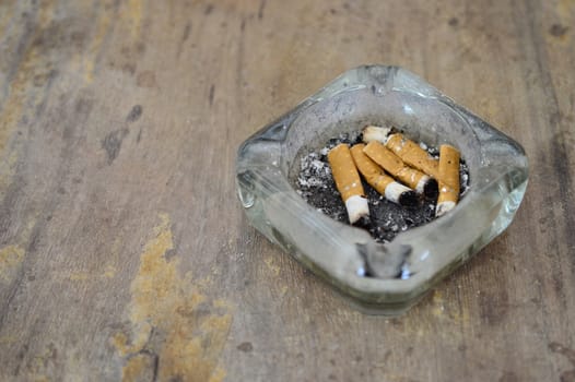 A dirty ashtray with cigarette ash and butts on dirty wooden