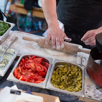 Chef making pita bread for falafel roll outdoor on street stall on Open kitchen international food festival event in Ljubljana, Slovenia. Street food ready to serve on a food stall.