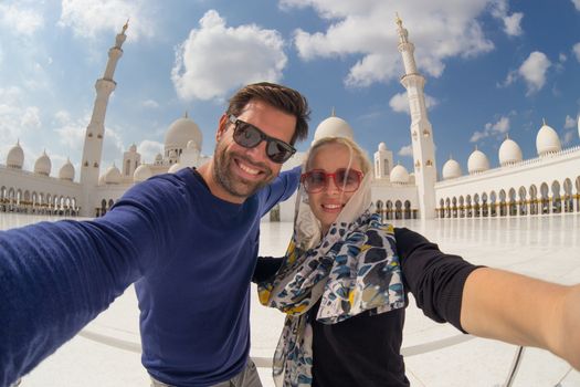 Tourist couple taking selfie in the courtyard of famous Sheikh Zayed Grand Mosque in Abu Dhabi, United Arab Emirates.